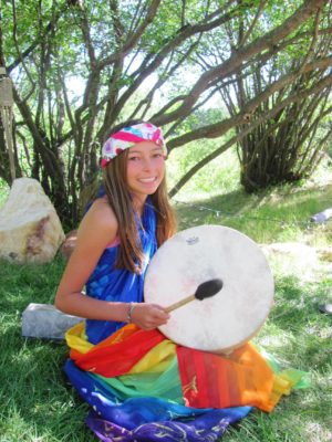young girl in colorful dress beating drum outside, nature retreat
