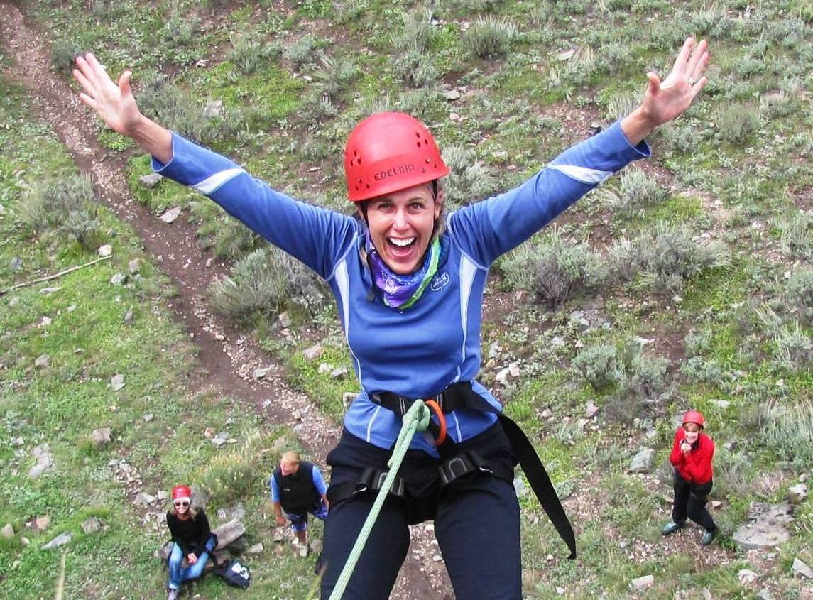 woman repelling down rock face with other women under her for support